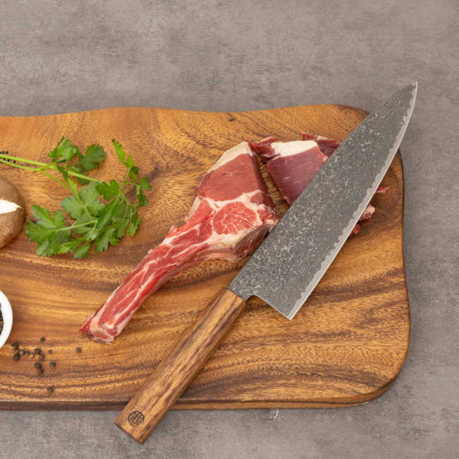 Damascus chef knife with wooden handle cutting raw meat on round wooden board