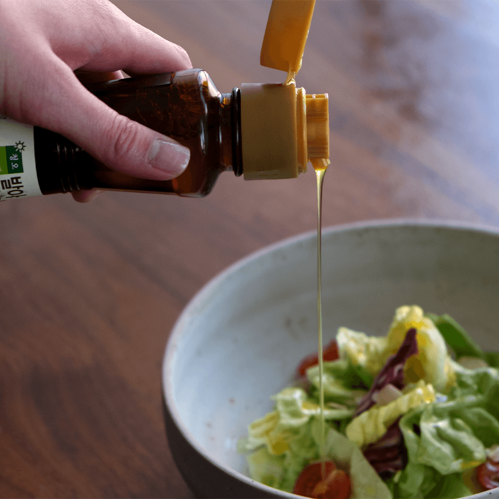 Bottle pouring sprouted perilla oil into a salad bowl