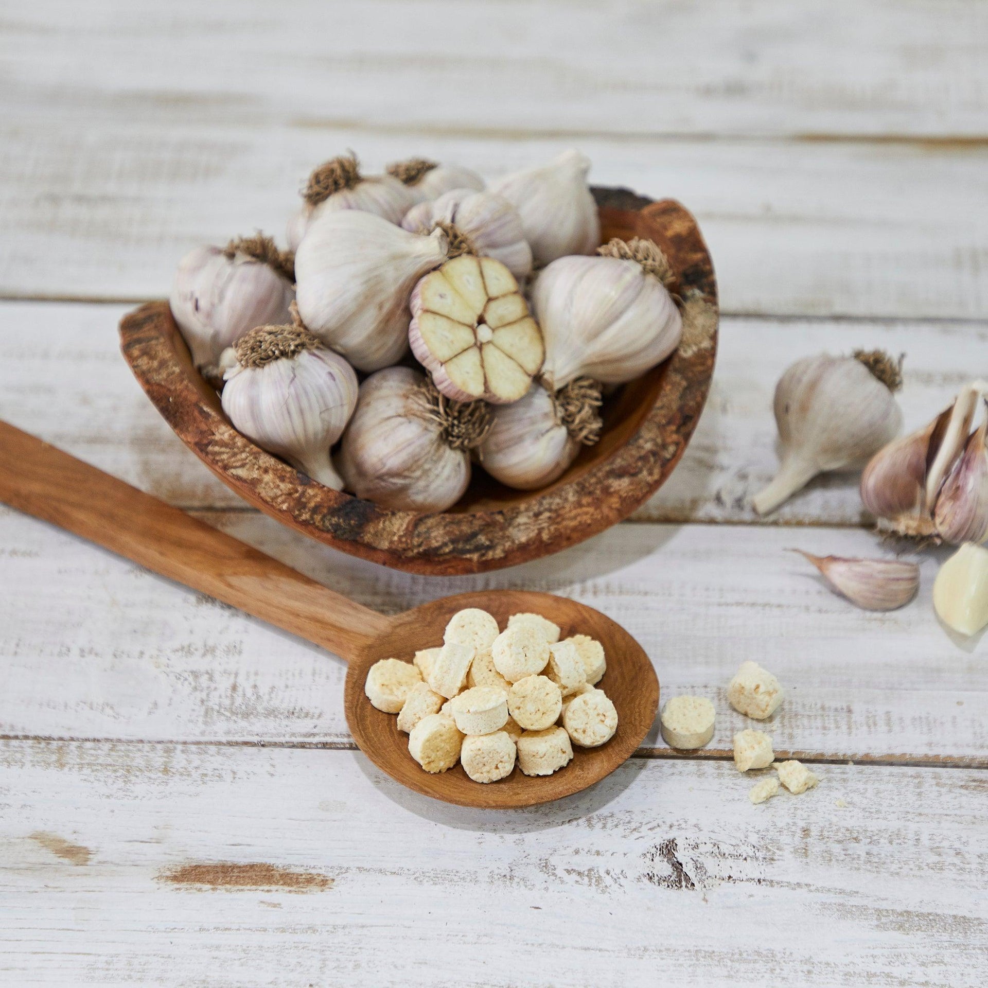 Garlic bulbs and chopped garlic tablets in wooden bowls and spoon