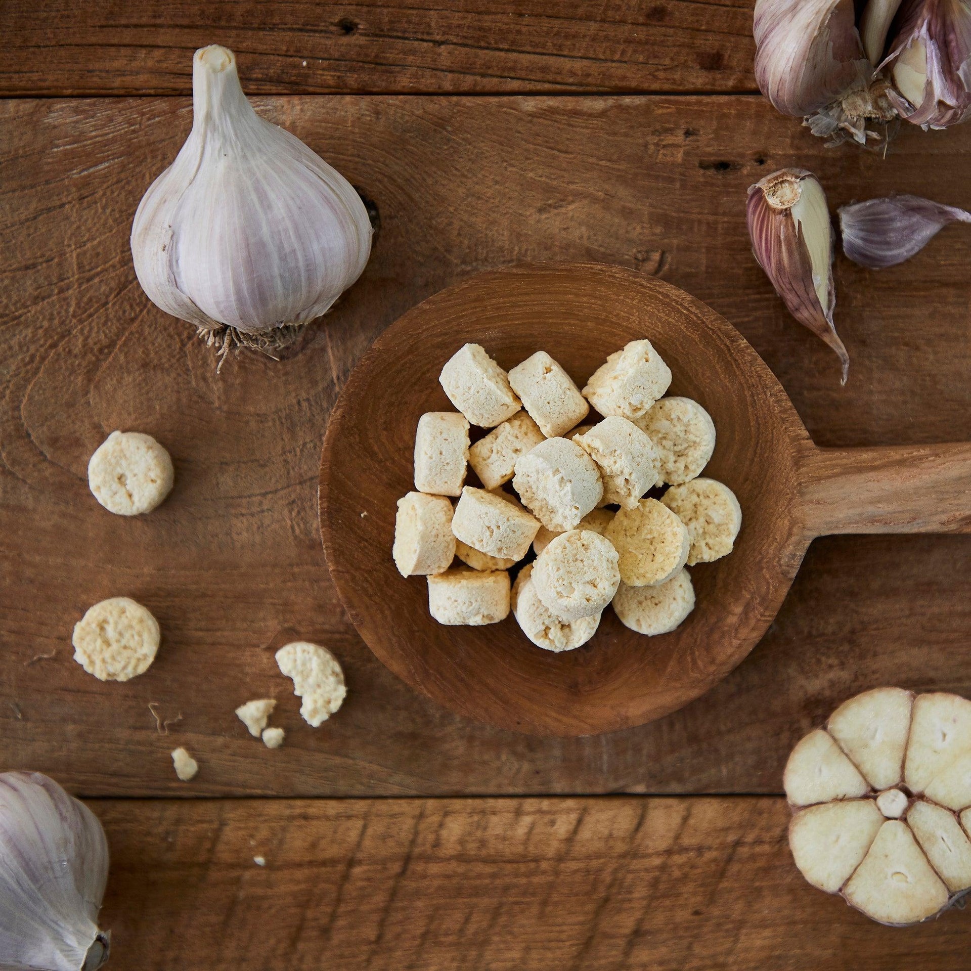 Chopped garlic tablets in round bowl with garlic cloves on wooden board