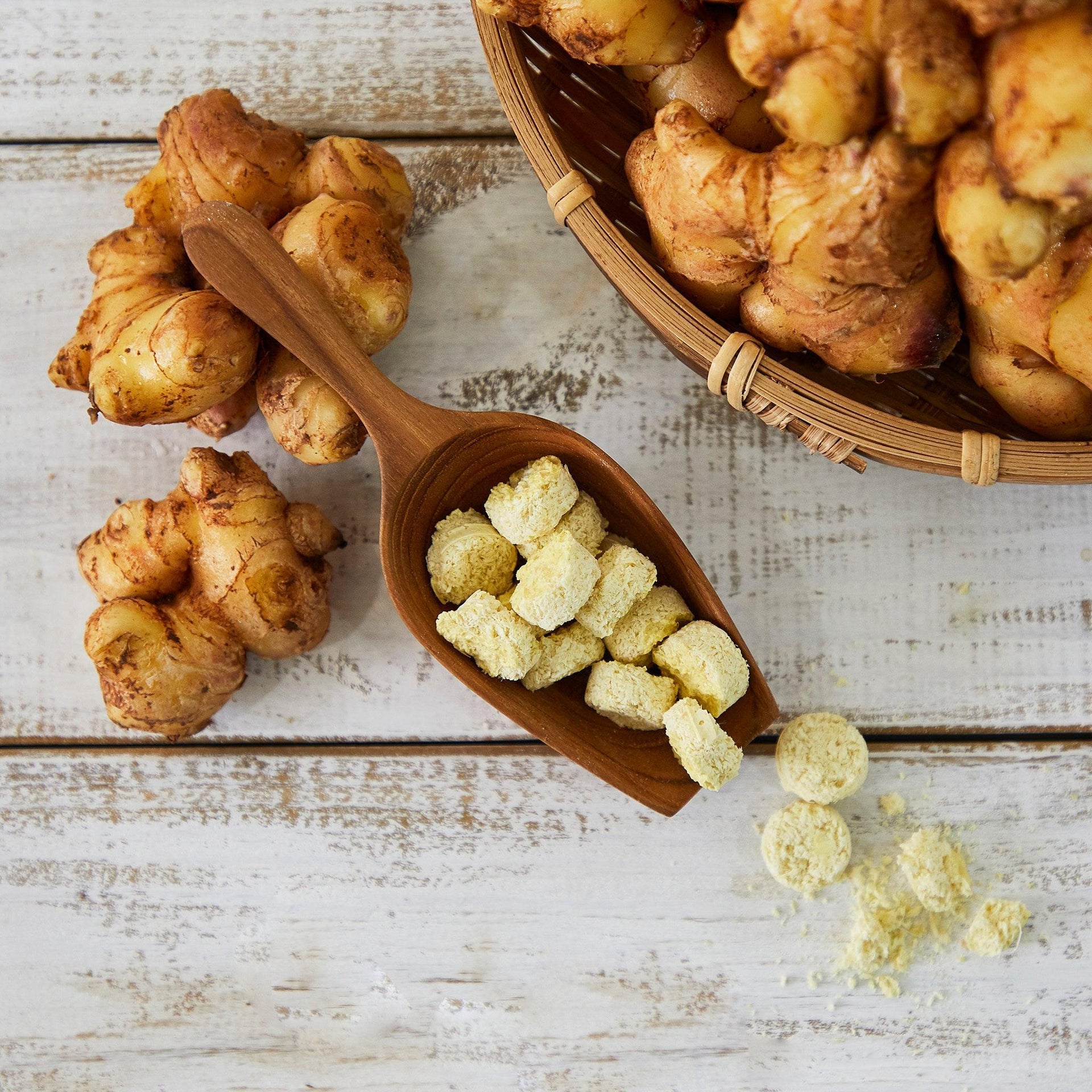 Freeze-dried minced ginger tablets in a wooden spoon with ginger roots nearby