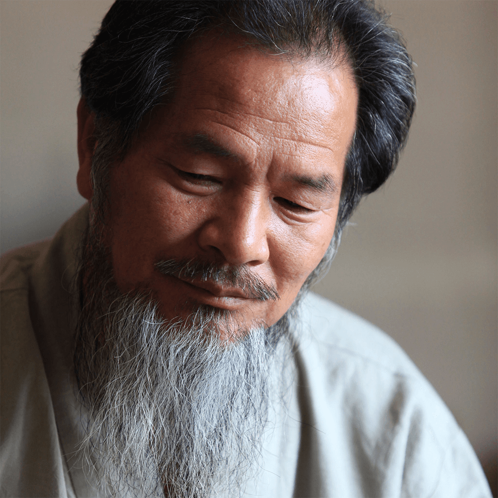 Elderly man with gray beard looking down, shown in close-up