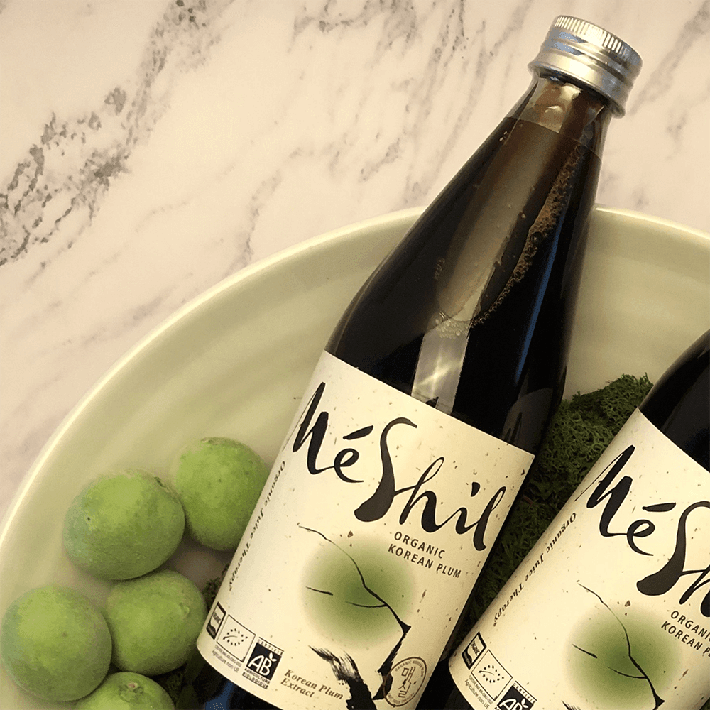 Organic Korean plum extract bottles with MeShil labels, shown with green apples