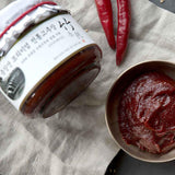 Jar of red gochujang chili paste with spoonful in metal bowl on fabric