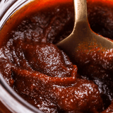 Gochujang paste spoon with thick red-brown chili sauce in a metal bowl